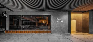 Modern minimalist restaurant entrance with concrete walls, glass doors, and wooden seating.