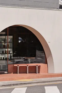 A minimalist storefront with a concrete entrance and glass windows, featuring a curved doorway and tiled floor.