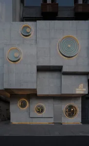 Modern concrete building facade with circular windows illuminated by warm lighting.