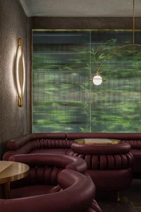 Modern interior design featuring curved leather sofas in front of a large, textured glass window showcasing green foliage.