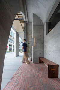 A modern concrete lobby with red brick flooring and a person walking by.