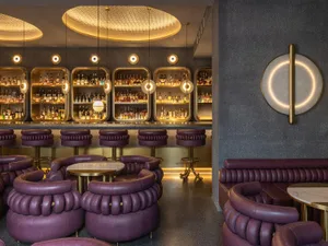 A modern bar interior featuring purple leather furniture and glass shelves filled with liquor bottles.
