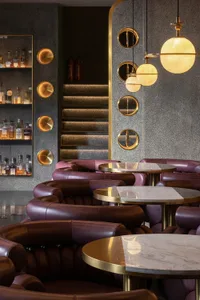 Interior design of a modern restaurant bar featuring leather seating, marble tables, and glass pendant lights.