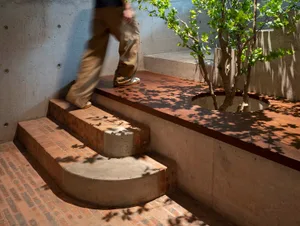A person walking on a wooden platform surrounded by green foliage and brick stairs.