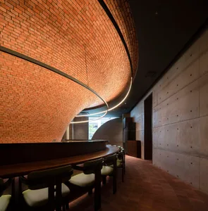 A modern, industrial-style restaurant interior featuring exposed brick walls and concrete elements, with a curved, brick-line