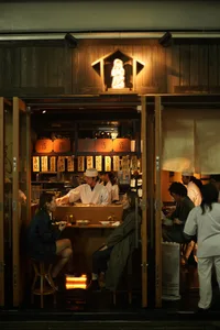 A cozy Japanese restaurant with wooden interiors and glass windows, illuminated by warm lighting.