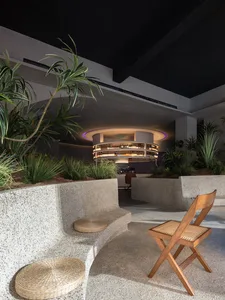 A modern bar interior featuring granite seating, concrete walls, and timber chairs with a circular bar counter in the backgro