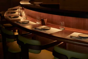 Modern restaurant bar with natural wood accents featuring green cushioned chairs and white table settings with glasses and pl