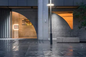 Modern storefront with curved concrete entrance and wooden interior, illuminated by warm lighting.