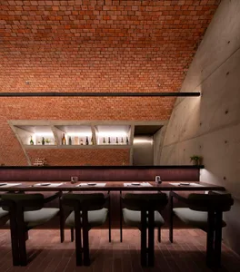 Industrial style restaurant interior with exposed brick ceiling, concrete walls, and a polished wooden table with place setti