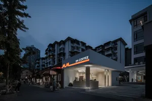 Nighttime view of a modern street-view coffee shop featuring concrete materials and illuminated signage.