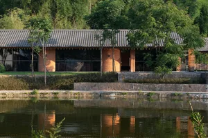 A modern residential building with brick walls and clay roof tiles reflected in a tranquil lake.