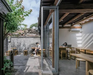 A modern coffee shop interior features large windows, wooden tables, and a concrete floor.