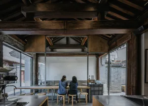 Two people sitting at a table in a modern interior coffee shop with wooden beams and large glass windows.