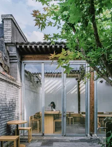 A modern coffee shop with wooden furniture and large glass doors, featuring a person working at a table inside.
