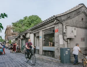 一條熱鬧的都市街道，兩旁是傳統磚造建築，人們步行或騎自行車穿梭其間。