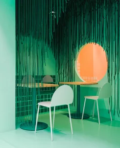 A modern, minimalist cafe interior with green tiles and white tables and chairs.