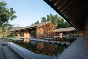 A minimalist residential building with bamboo structural elements and a serene courtyard with a reflective pond.