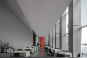 Modern restaurant with concrete walls, glass columns, and white tables and chairs.