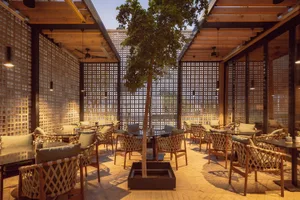 Industrially-styled coffee shop with metal and wooden furnishings and a central tree in a planter.