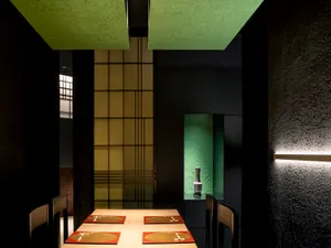Modern restaurant interior with wooden tables, red placemats, and a green wall with a vase.