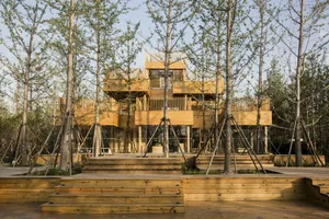 A modern treehouse with a wooden exterior surrounded by trees and wooden platforms.