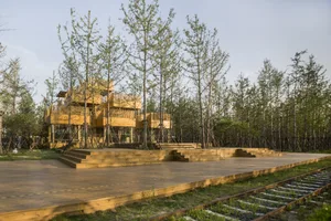 A wooden outdoor theatre surrounded by tall trees and railway tracks.