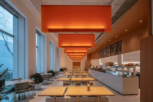 Modern cafe interior with orange lighting, tables, chairs, and menu board.