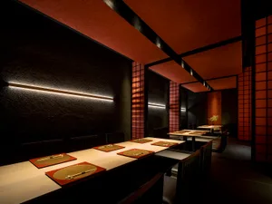 A modern restaurant interior with wooden tables, red place mats, and geometric lighting fixtures.