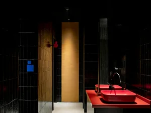 Modern restroom with sleek black tiles and vibrant red countertops, featuring red faucets and a unique, minimalist design.