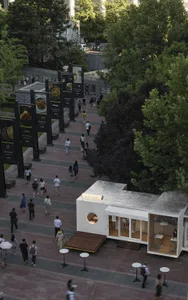 Outdoor area of a street-side cafe with metal exterior, surrounded by greenery and pedestrian walkways.
