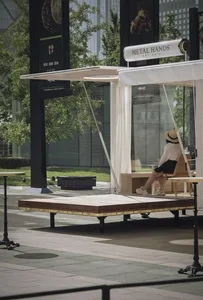 A minimalist urban cafe with wooden platforms, metal seating, glass walls, and fabric curtains.
