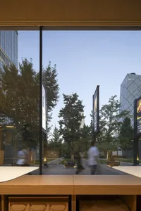 Outdoor urban space with glass buildings, wooden tables, and concrete pathways.