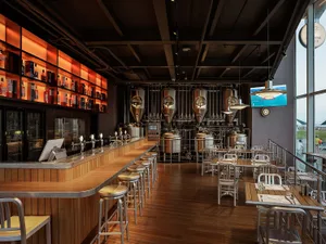 Industrial-themed restaurant bar with wooden tables, metal stools, and glass brewing tanks.