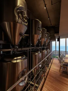 Modern brewery with metal containers and a wooden deck overlooking the ocean.