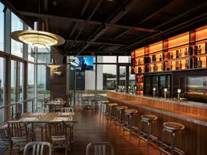 Modern restaurant interior featuring a bar area with concrete and wood finishes, and wooden bar stools.
