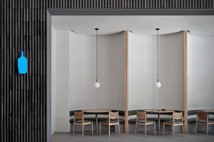 A minimalist cafe interior with concrete walls, round wooden tables, and wooden chairs.