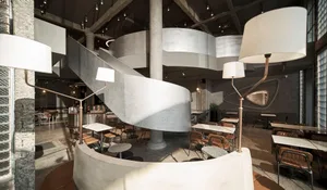 Concrete and steel industrial-style restaurant interior with spiral staircase and multiple seating areas.