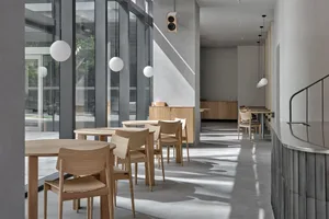 A modern cafe space featuring concrete walls, wooden tables, and glass windows.