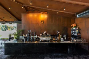 Modern coffee shop interior featuring a sleek metal and concrete counter with coffee-making equipment.