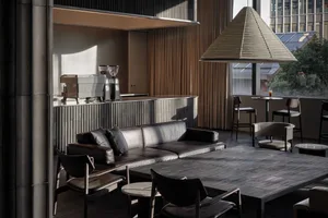 Modern coffee shop interior design featuring black leather sofas and metallic furniture against concrete walls.