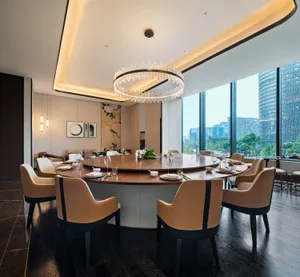 Modern dining room featuring a round wooden table with leather chairs and a large glass chandelier.