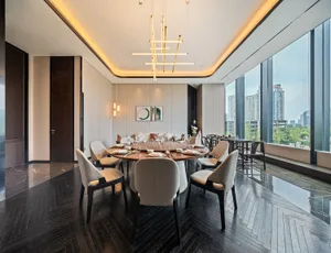 Modern dining room featuring a wooden table surrounded by leather chairs, with a sleek lighting fixture and large windows ove