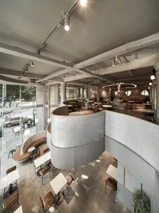 A modern, minimalist coffee shop with concrete walls and floor, featuring contemporary furniture and a spacious, open layout.