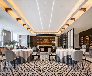 A modern restaurant interior with marble patterned floor, white tablecloths, and gray chairs.