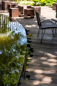 A wooden patio by a pond, featuring modern furniture and natural surroundings.
