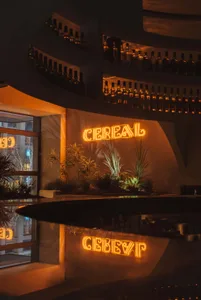 An illuminated neon sign reading 'CEREA', featuring a bar counter with neon lighting and various plants.