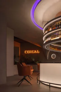 A modern restaurant bar with concrete walls, illuminated by neon signs, featuring a stylish seating area with orange chairs a