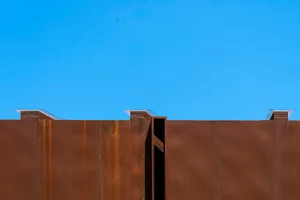 Rusty metal exterior wall with three ventilation hatches against a clear blue sky.