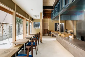 Industrial-style restaurant interior featuring wooden furniture, concrete flooring, and glass elements.